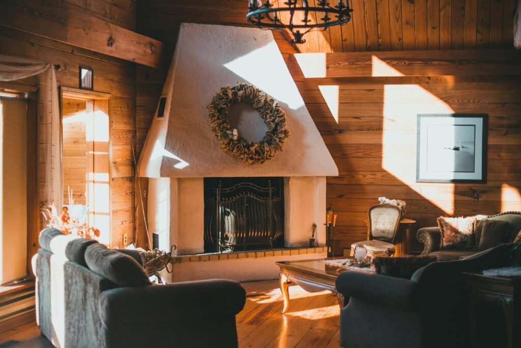 Sunlit rustic living room with wooden walls, cozy furnishings, and a fireplace for a warm ambiance.
