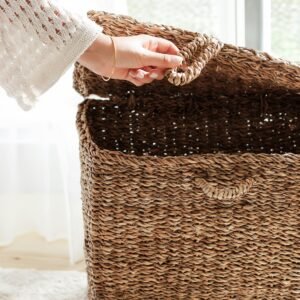 Hand opening a woven wicker basket in a sunlit indoor space, suggesting organization and home decor.