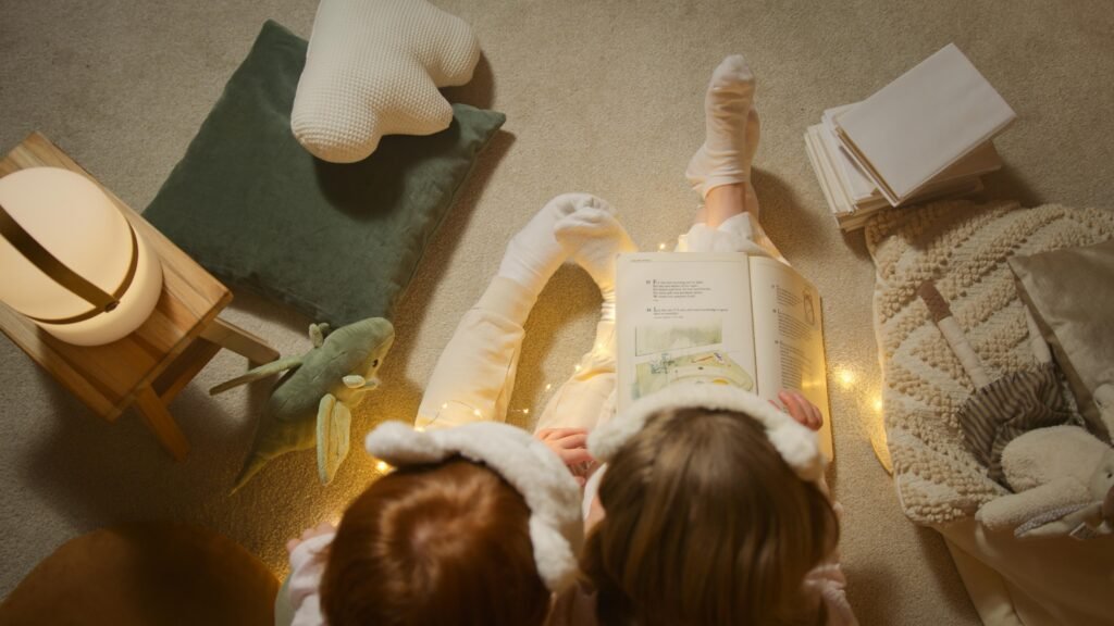 Two children in pajamas reading a book together at bedtime with soft lighting and toys around.